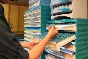 white person pulling out drawer with many small items and holding one in hand